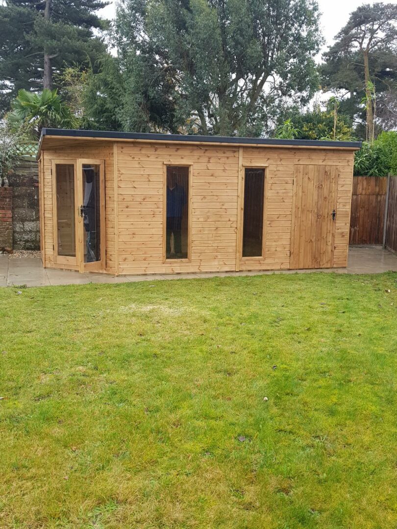Wooden garden room with tall windows and side storage section, set on paving with lawn and trees in the background