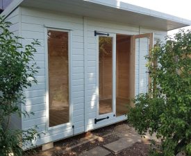White-painted garden studio with tall glass doors and windows, flat roof, and timber interior, surrounded by plants