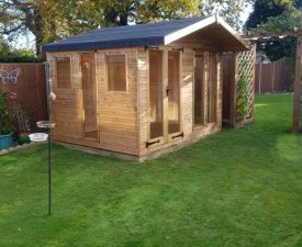 Wooden garden office studio with windows and double doors, surrounded by green lawn and trees in autumn